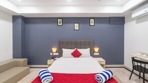 Quarto de hotel moderno com cama, mesas de cabeceira, escrivaninha e uma cadeira.