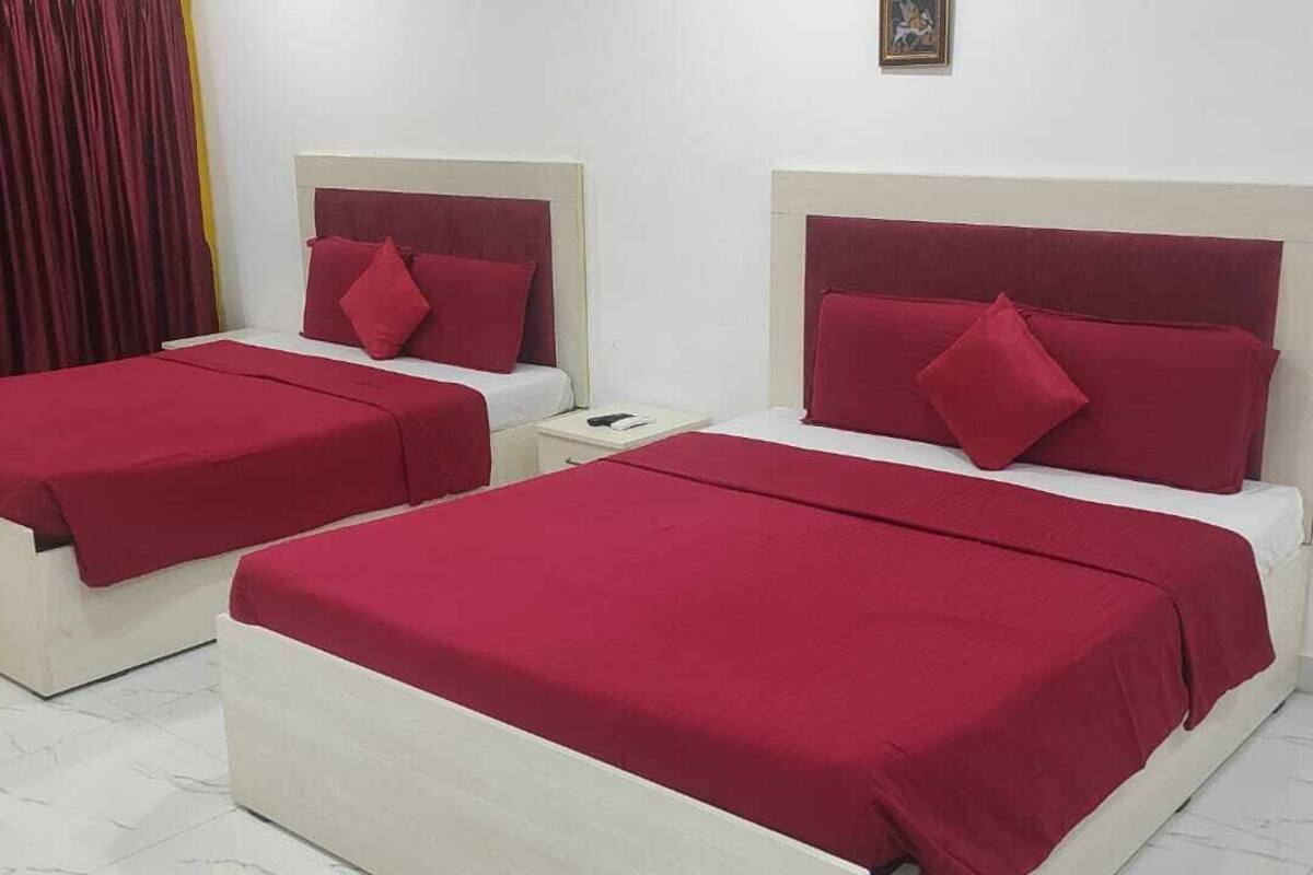 Two twin beds with red bedding, white headboards, and a small bedside table with a book.