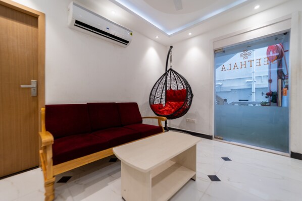 A modern interior with a red sofa, a hanging chair with a red cushion, a wooden table, and a glass door with a view of the outside.