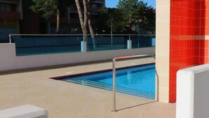 A swimming pool with a metal safety railing, surrounded by a tiled deck and a red wall. - Enjoy Poolside Comfort-beahost (San Michele al Tagliamento)