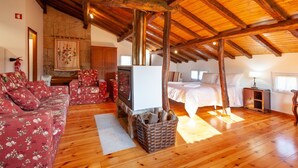 A cozy room with a wooden ceiling, a fireplace, a bed, a sofa, and a television. - Loft Casinha - old barn in a rural area (Caminha)