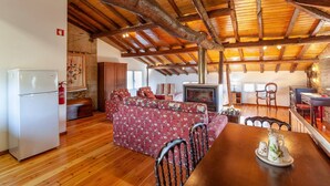 A rustic interior with a wooden ceiling, a sofa set, a dining table, and a fireplace. - Loft Casinha - old barn in a rural area (Caminha)