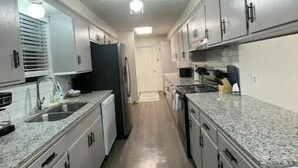 A narrow kitchen with white cabinets, a granite countertop, and a central island. - Quick Access/ Sleeps 10/ Pets Ok (Portland)