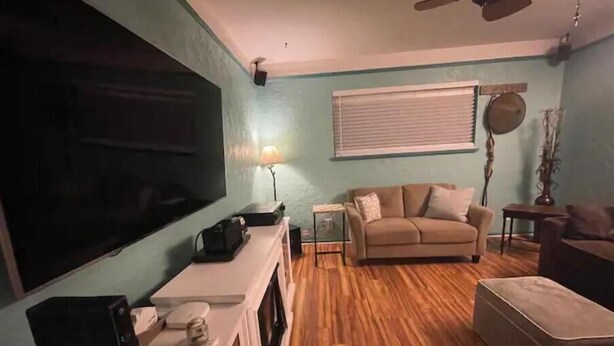 A living room with a large flat-screen TV, a sofa, a coffee table, and a ceiling fan.