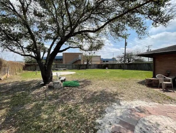 Un patio trasero con un árbol grande, un patio de ladrillo y una zona verde.