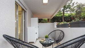 A balcony with three black wicker chairs, a small table with a glass, a plant, and a white cabinet. -  Mystique One Bedroom Apartment by BluPine (Vari-Voula-Vouliagmeni)