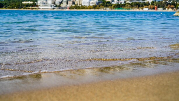 A beach with clear water and a distant view of buildings. -  Mystique One Bedroom Apartment by BluPine (Vari-Voula-Vouliagmeni)