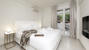 A modern hotel room with a large bed, a bedside table with a lamp, a view of the outdoors through a sliding glass door, and a flat-screen TV on the wall. -  Mystique One Bedroom Apartment by BluPine (Vari-Voula-Vouliagmeni)