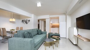 A modern living room with a green sofa, a dining table with chairs, and a kitchen area in the background. -  Mystique One Bedroom Apartment by BluPine (Vari-Voula-Vouliagmeni)