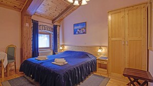 A wooden room with a large bed, a wooden wardrobe, a small table, and a chair.