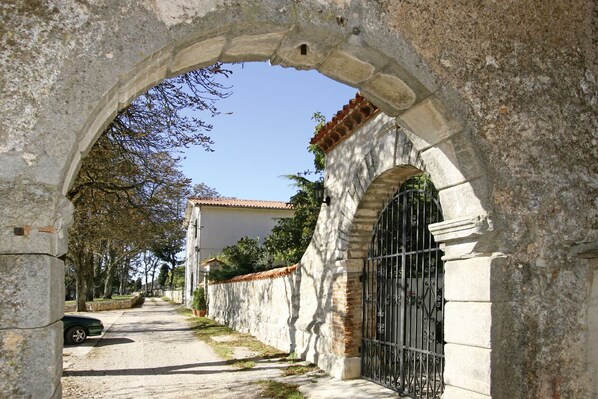 An arched stone gateway leading to a building with a metal gate, a paved path, and a parked car.