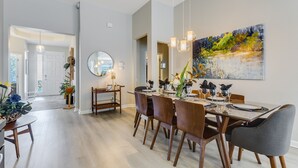 A modern dining area with a large table, multiple chairs, and hanging pendant lights.