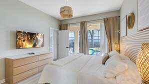 A bedroom with a bed, a television, a dresser, and a view of the outdoors.