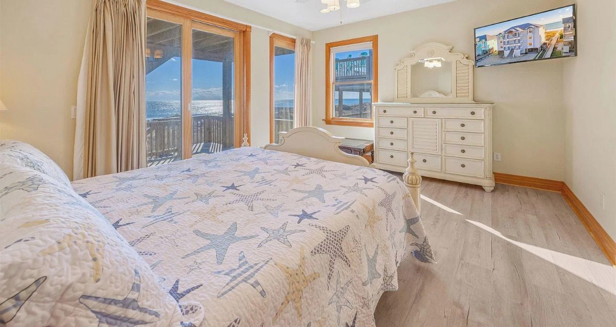 Quarto com cama, cômoda, televisão e varanda com vista.