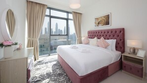 A modern hotel room with a large bed, a city view, a round mirror, and a bedside table with a lamp. - Luxury StayCation - Beachfront Apartment With Fantastic Palm Views  (Dubai)