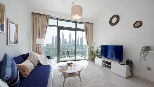 A modern living room with a sofa, coffee table, TV, and a balcony with a city view. - Luxury StayCation - Beachfront Apartment With Fantastic Palm Views  (Dubai)