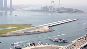 A coastal cityscape with a prominent Ferris wheel, a marina with boats, and modern buildings. - Luxury StayCation - Beachfront Apartment With Fantastic Palm Views  (Dubai)