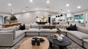 A modern living room with a sectional sofa, a wooden coffee table, and a kitchen in the background. - Scottsdale Clubhouse | Pool, Spa & Golf Simulator (Scottsdale)