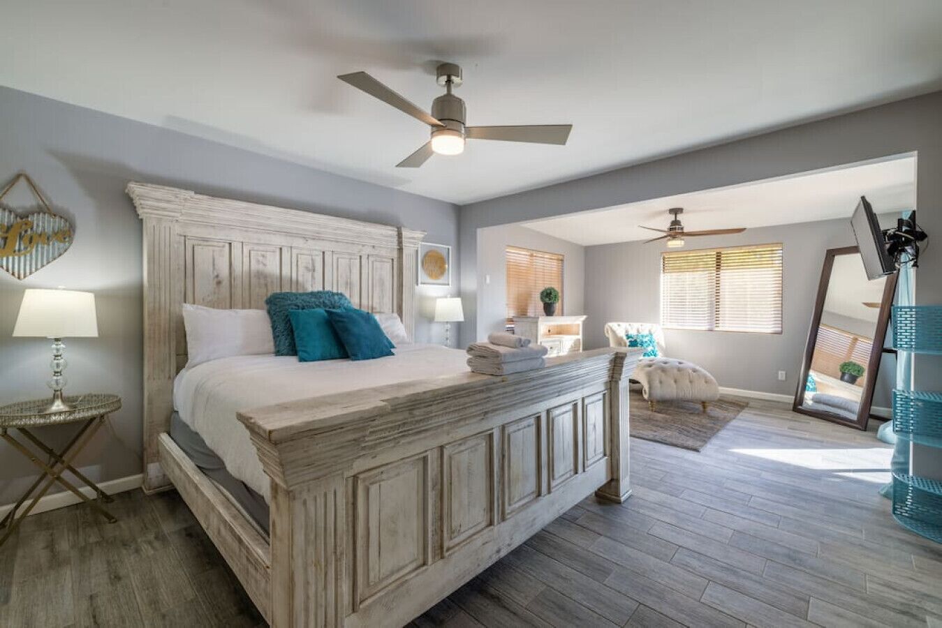 Quarto com cama grande, ventoinha no teto, mesa de cabeceira, cadeira e espelho.