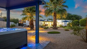 A modern outdoor patio area with a hot tub, palm trees, and a covered seating area.
