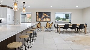 A modern kitchen with a central island, bar stools, a dining table with chairs, and a large painting of a horse.