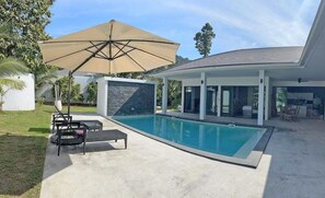 Una casa moderna amb piscina, mobiliari d'exterior i un gran parasol.
