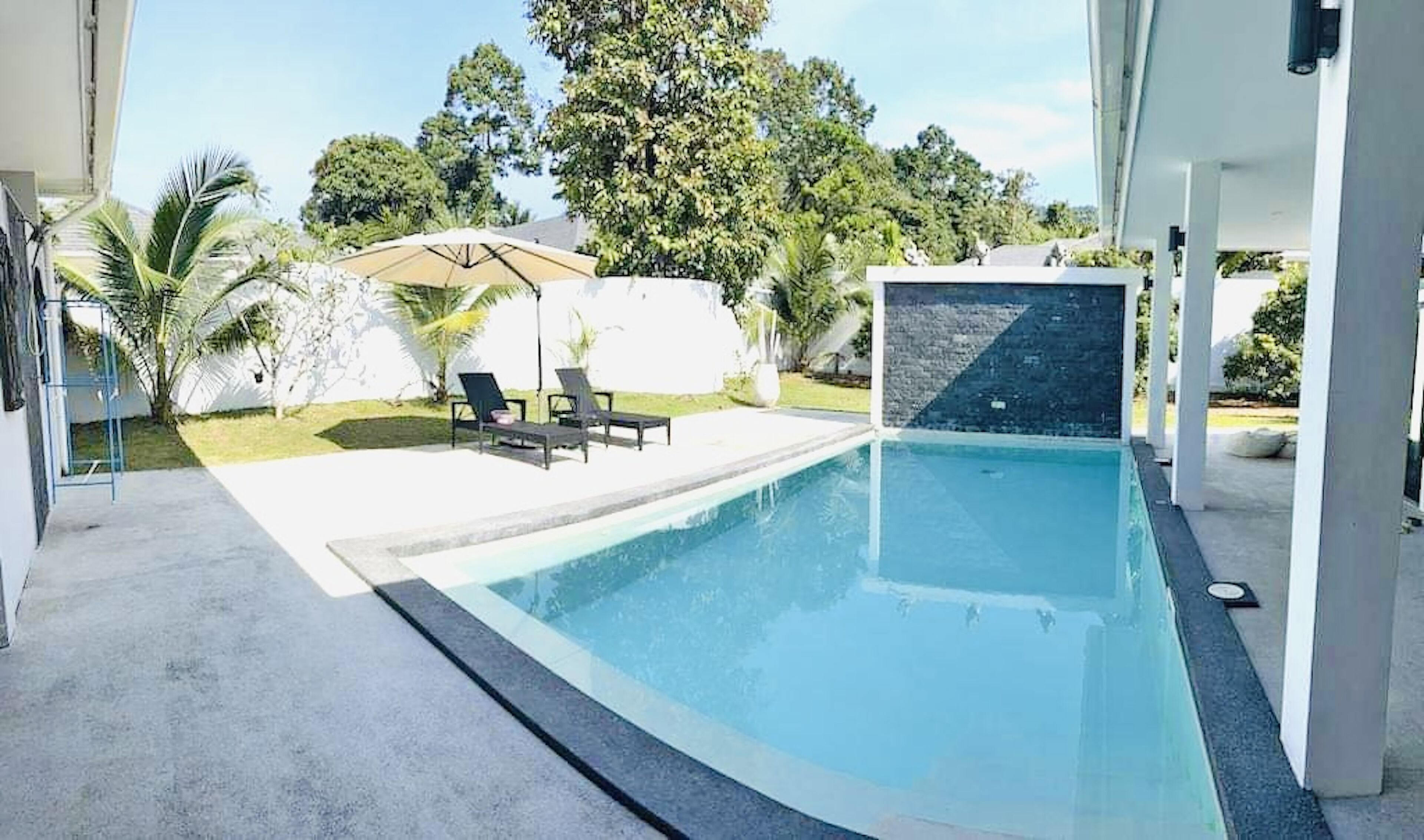 Un área de piscina exterior moderna con una vista despejada del cielo, rodeada de vegetación exuberante y palmeras.