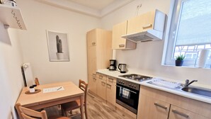 A compact kitchen with wooden cabinets, a stove, a sink, and a window with a view. - P2 Schönes Apartment in Fuldatal (Fuldatal)