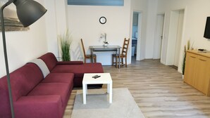 A living room with a red sofa, a white coffee table, a floor lamp, and a dining area with a table and chairs. - P2 Schönes Apartment in Fuldatal (Fuldatal)