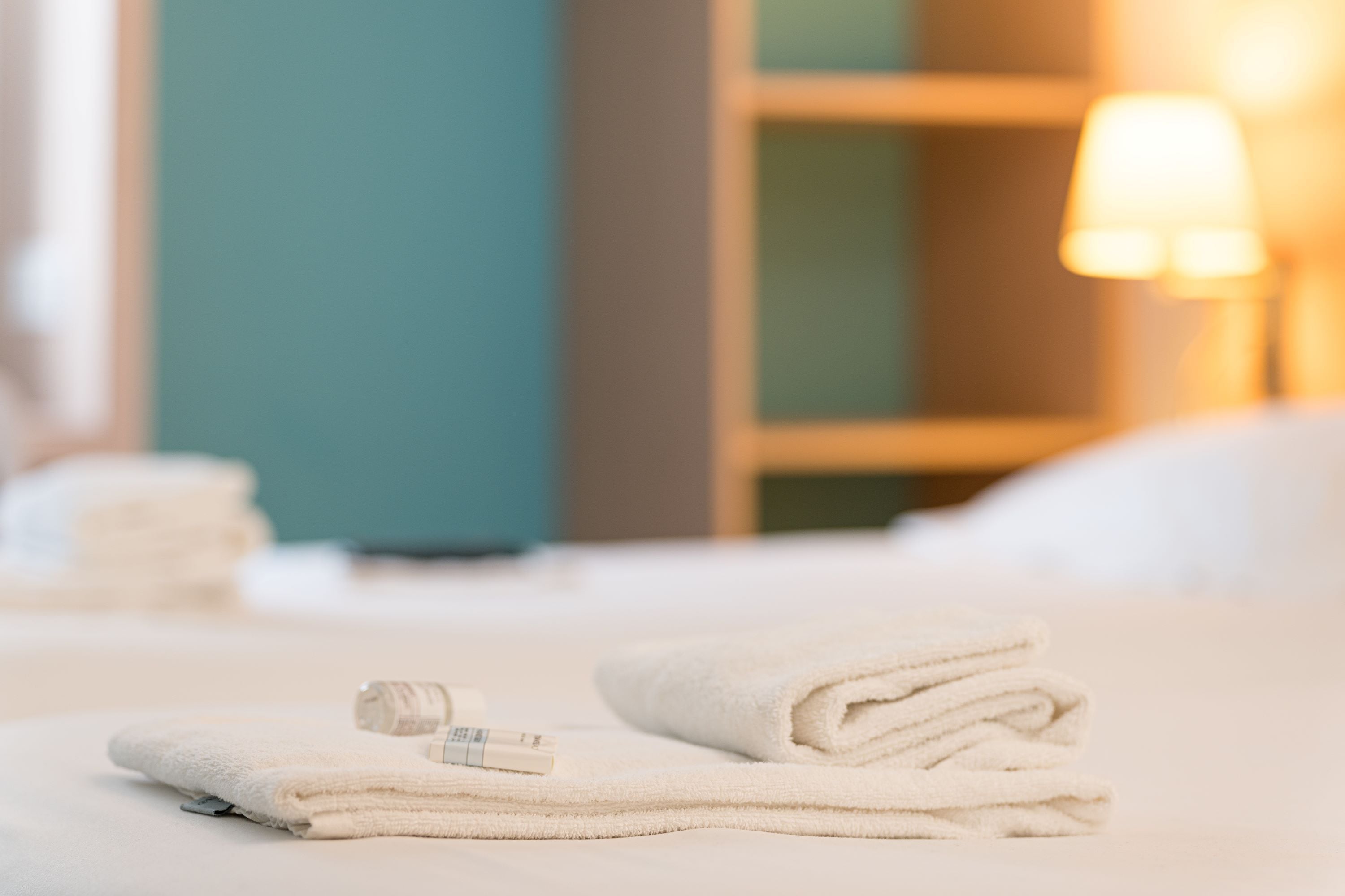 Een opgemaakt bed met gevouwen handdoeken en een flesje lotion erop.