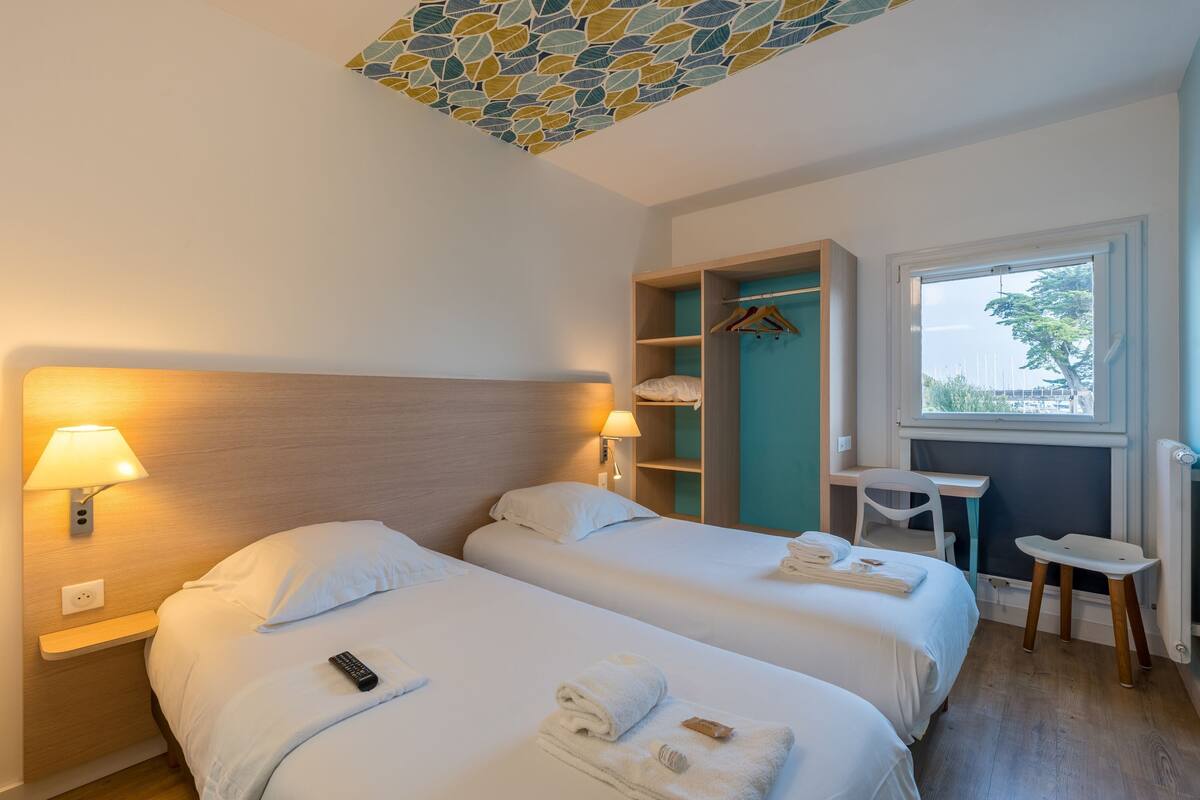 Habitación de hotel con dos camas, un escritorio, una silla y un armario.