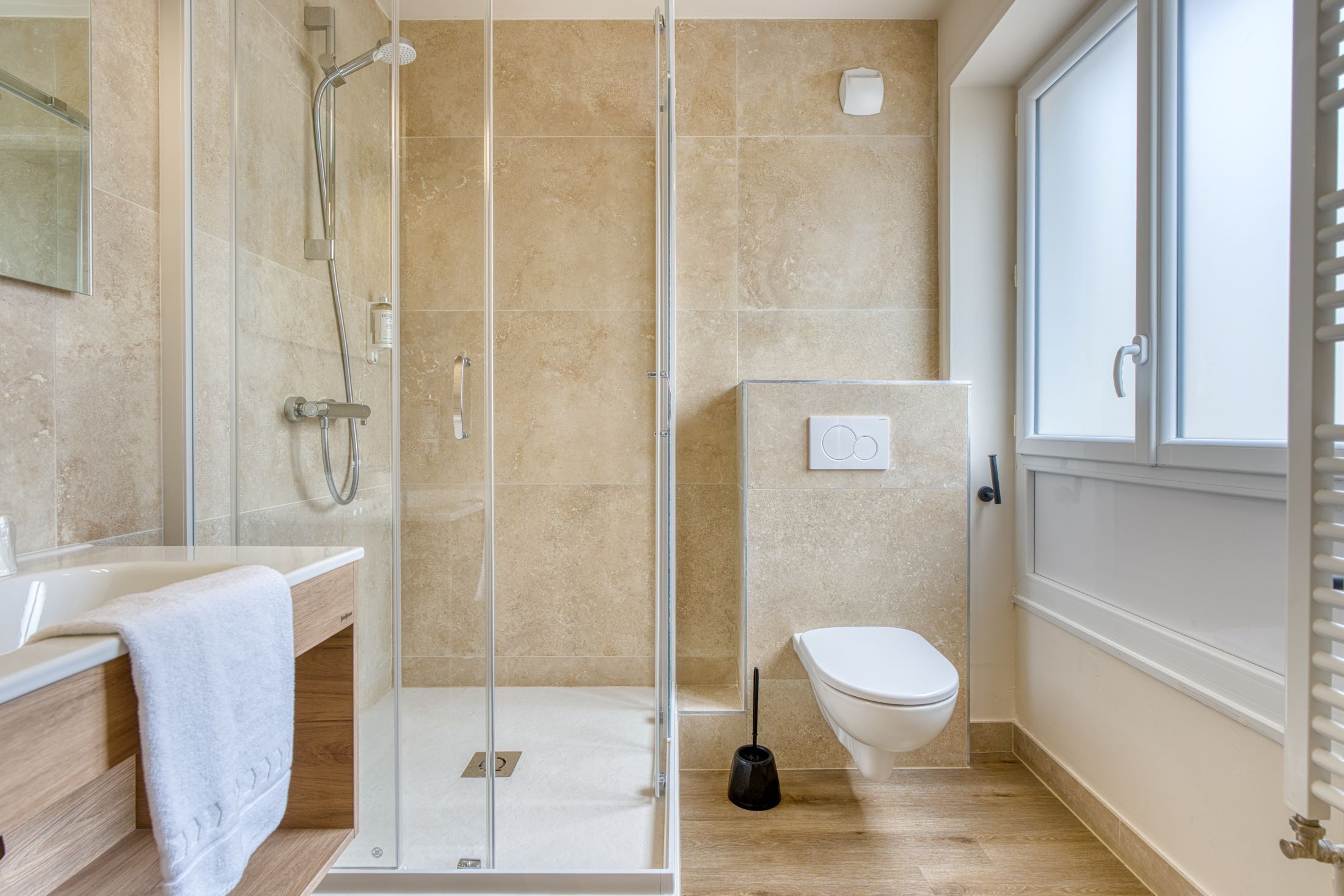 A modern bathroom with a glass shower enclosure, a white toilet, and a wooden vanity with a towel.