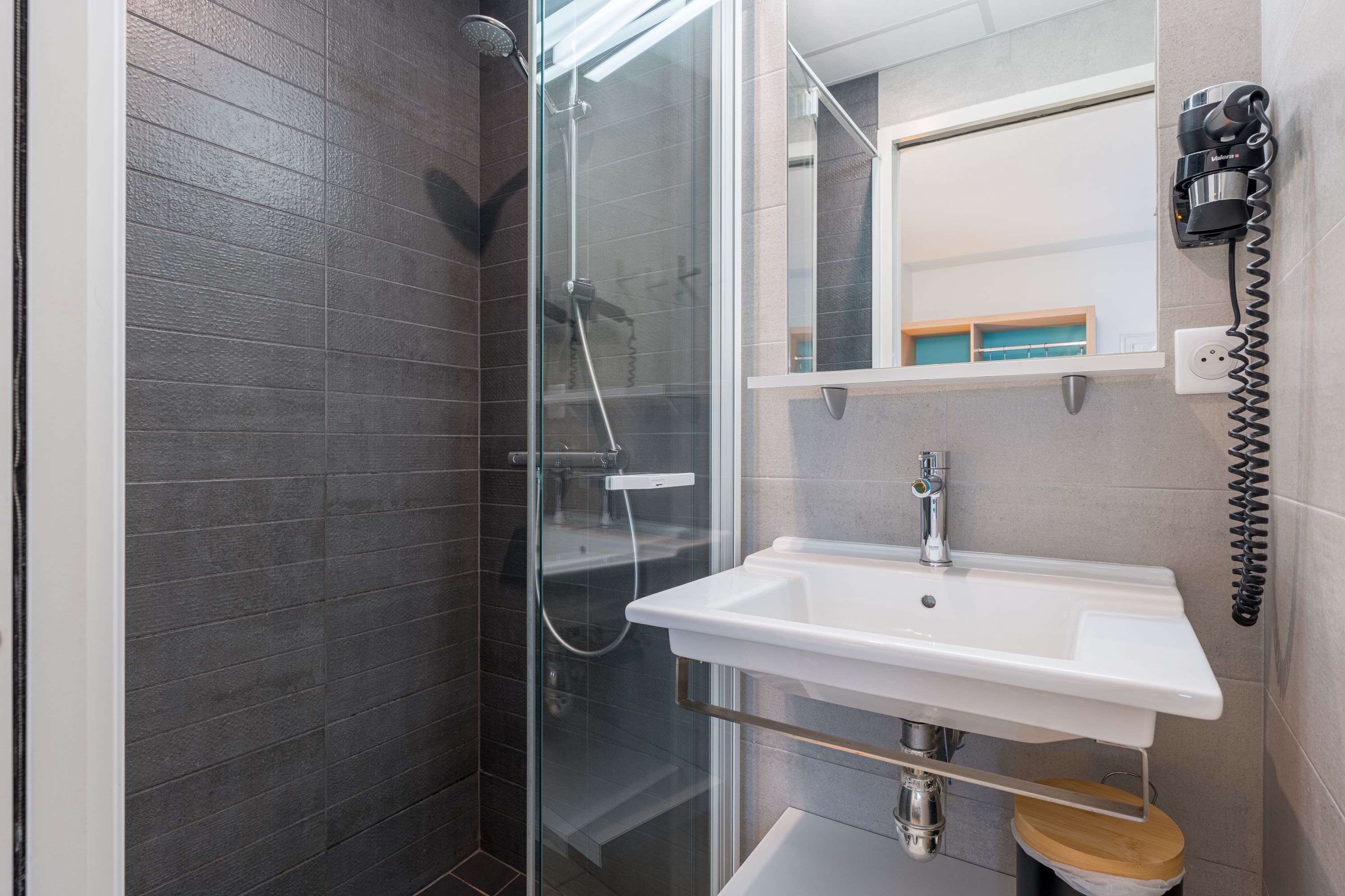 A modern bathroom with a glass shower enclosure, a white sink, and a mirror above the sink.