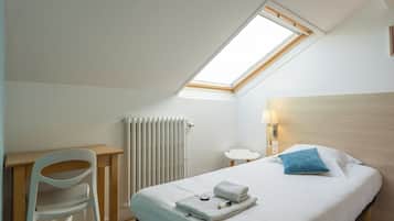 Um quarto com claraboia, cama com travesseiro azul, mesa de cabeceira com abajur e radiador.