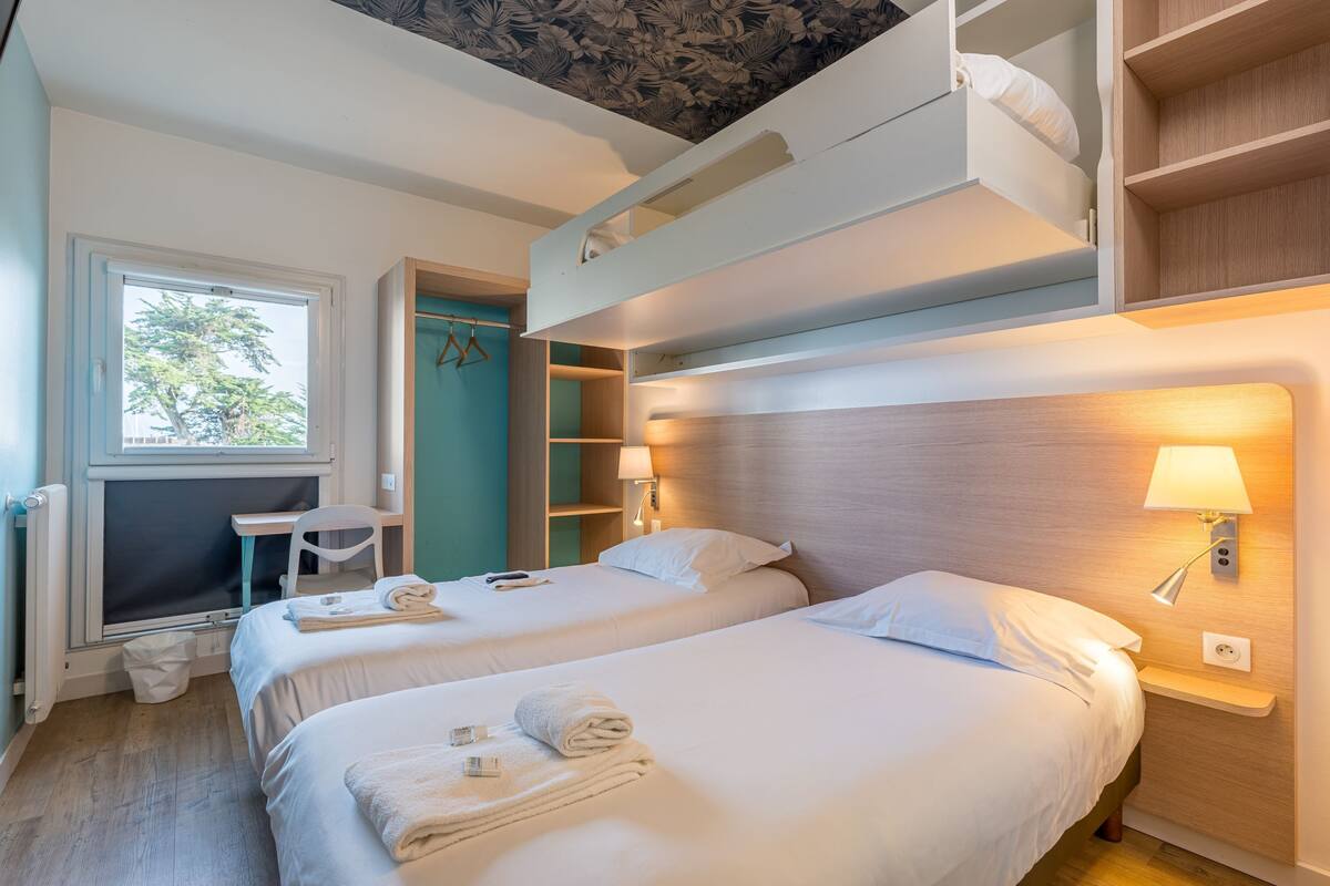 Habitación de hotel con dos camas, un escritorio, una silla y una cama alta.