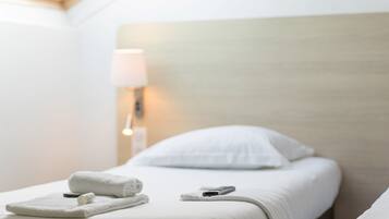 Una cama bien hecha con sábanas blancas, una toalla enrollada y un control remoto sobre la cama.