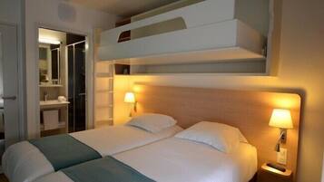 A hotel room with two beds, a bunk bed above, a bathroom with a mirror, and two bedside lamps.