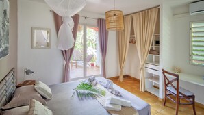 A bedroom with a bed, a chair, a desk, and a window with curtains. - Villas "les Saintes" Pour 4 à 5 Personnes à 50 m de la Plage au Calme (Saint-François)
