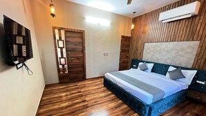 Ein Schlafzimmer mit Holzboden, einem Bett mit blauer Kopfteil, einem an der Wand montierten Fernseher und einer Klimaanlage.