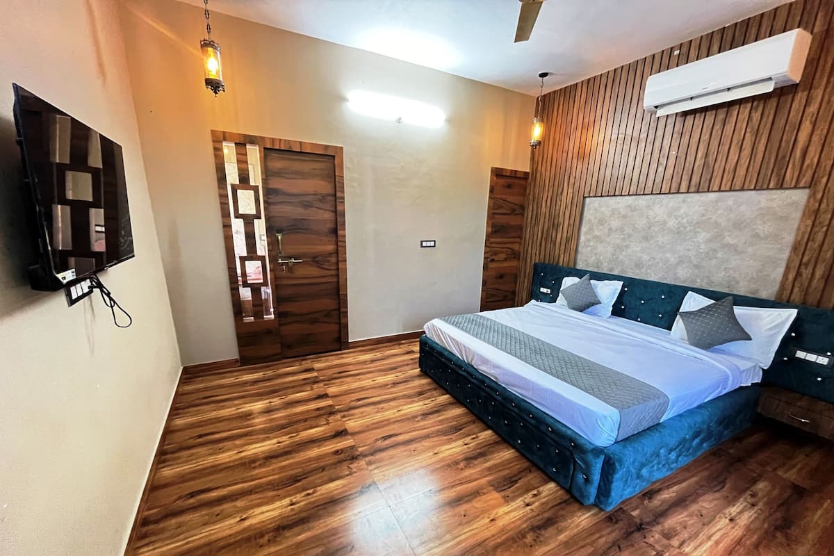 A bedroom with a wooden floor, a bed with a blue headboard, a wall-mounted TV, and an air conditioning unit.