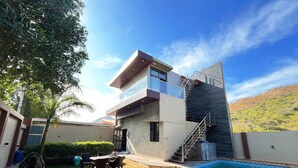 Ein modernes, zweistöckiges Haus mit Pool, Außenbereich und einer Treppe zu einem Balkon.