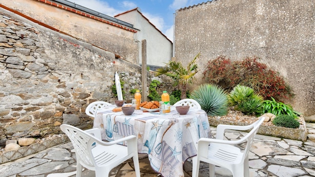 A stone wall, a white table with a tablecloth, and a variety of plants. - Town centre - House for 4 with beautiful courtyard (Noirmoutier-en-l´Ile)
