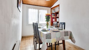 A dining area with a table set for four, a bookshelf, and a window with curtains. - Town centre - House for 4 with beautiful courtyard (Noirmoutier-en-l´Ile)