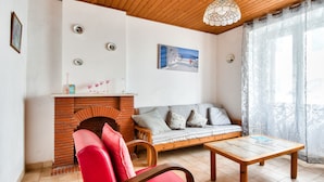 A living room with a brick fireplace, a wooden ceiling, a sofa with cushions, a red chair, and a table. - Town centre - House for 4 with beautiful courtyard (Noirmoutier-en-l´Ile)