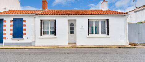 A white building with a red-tiled roof, two windows, and a door.