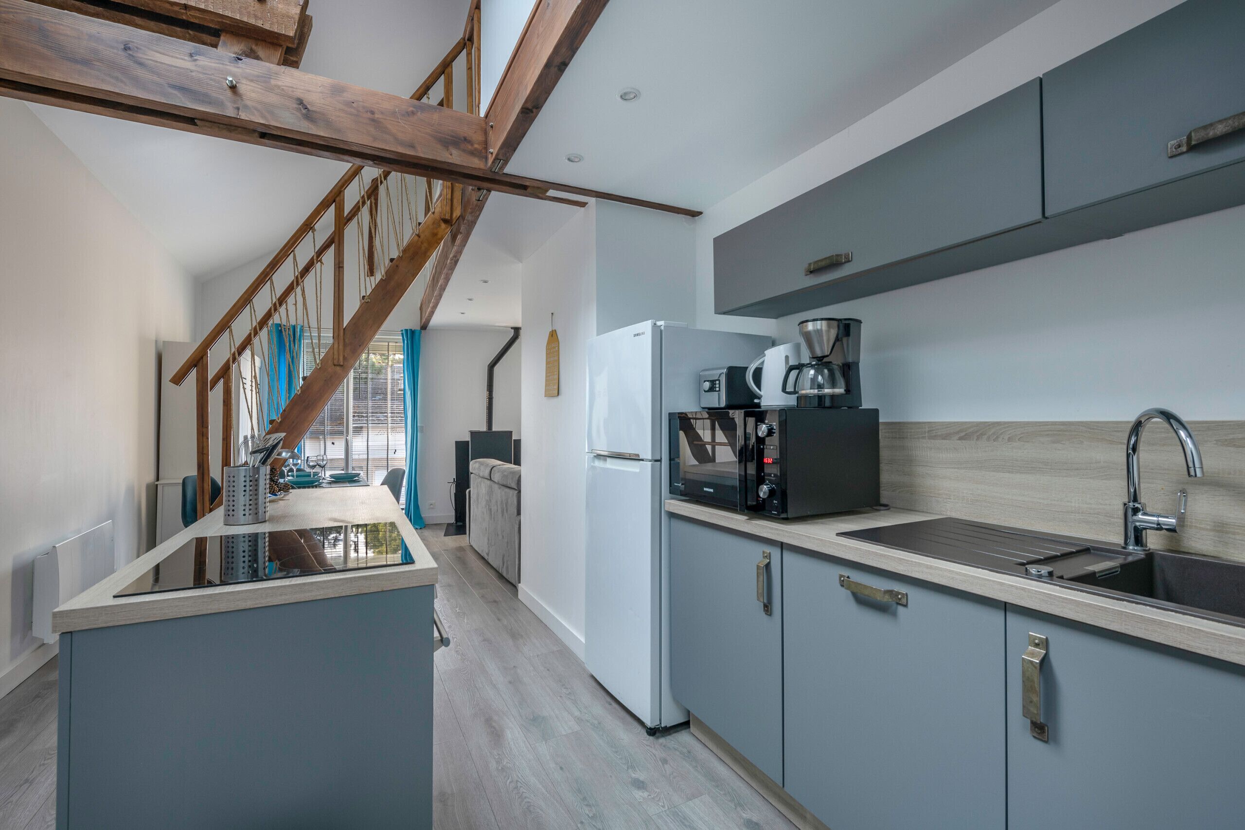 Une cuisine moderne avec un escalier en bois, un réfrigérateur blanc, une machine à café et un évier.