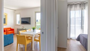 A room with a dining table, chairs, a TV mounted on the wall, and a bed with a window.