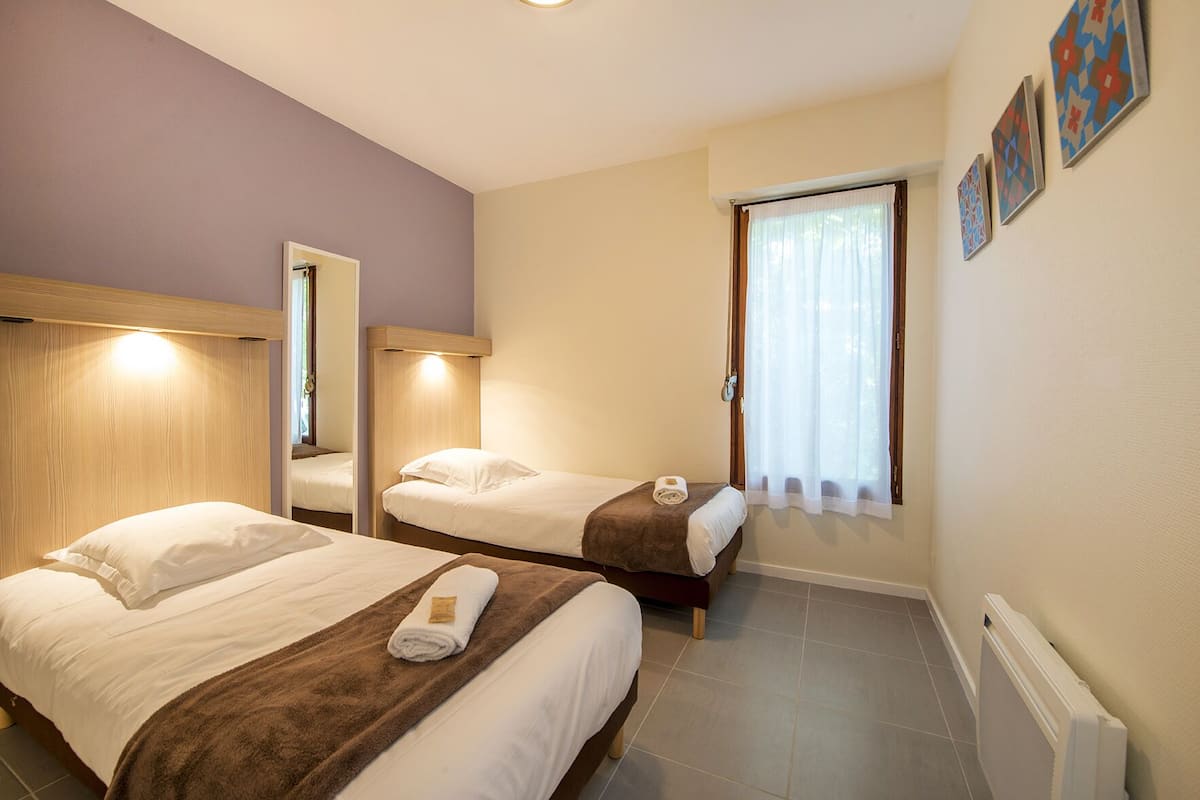 A hotel room with two beds, a window with curtains, and a radiator.