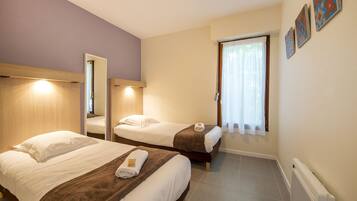 A hotel room with two beds, a window with curtains, and a radiator.