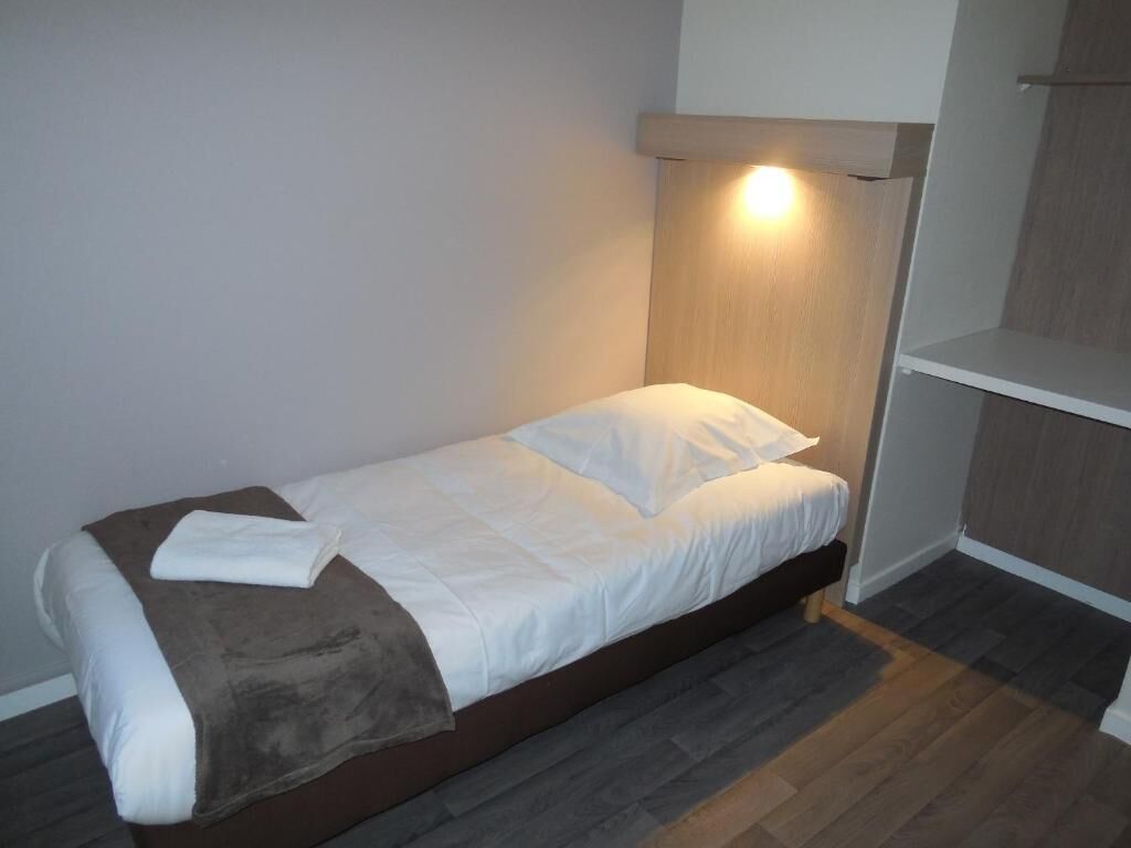 Ein Einzelbett mit Kopfteil, einem weißen Kopfkissen und einer braunen Decke.